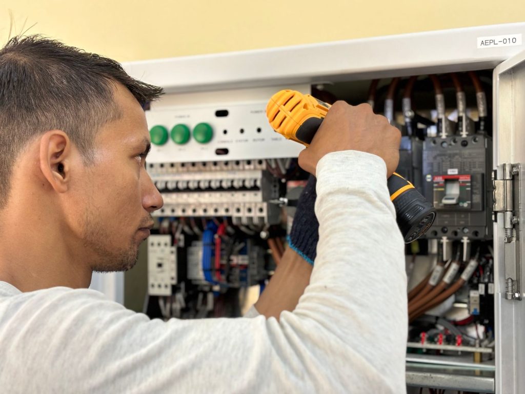 Electrician using a drill on a circuit breaker panel during installation
