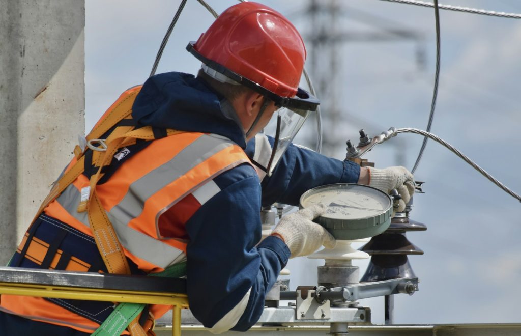 Electrician wearing a red safety helmet and hi-vis vest testing electrical equipment