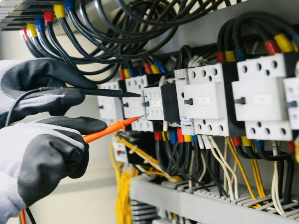 Electrician testing contactors inside an electrical panel with a multimeter probe
