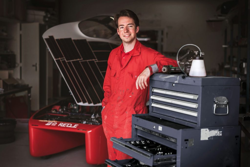 Technician in red overalls standing beside a tool chest in a workshop