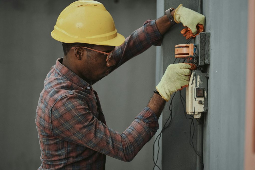 Electrician in a plaid shirt and hard hat holding tools while working on a panel
