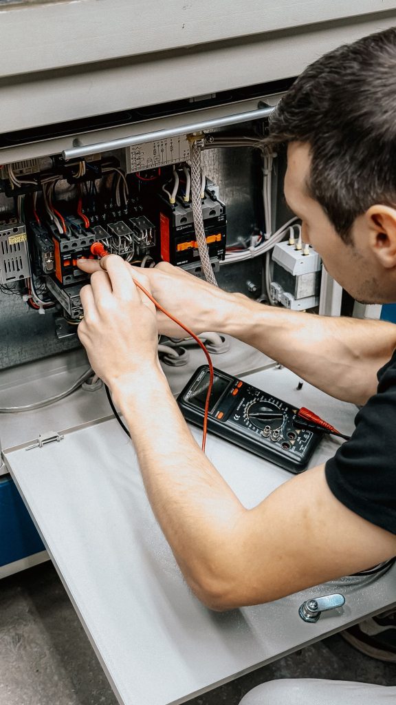 Technician checking connections inside an open electrical panel with a multimeter